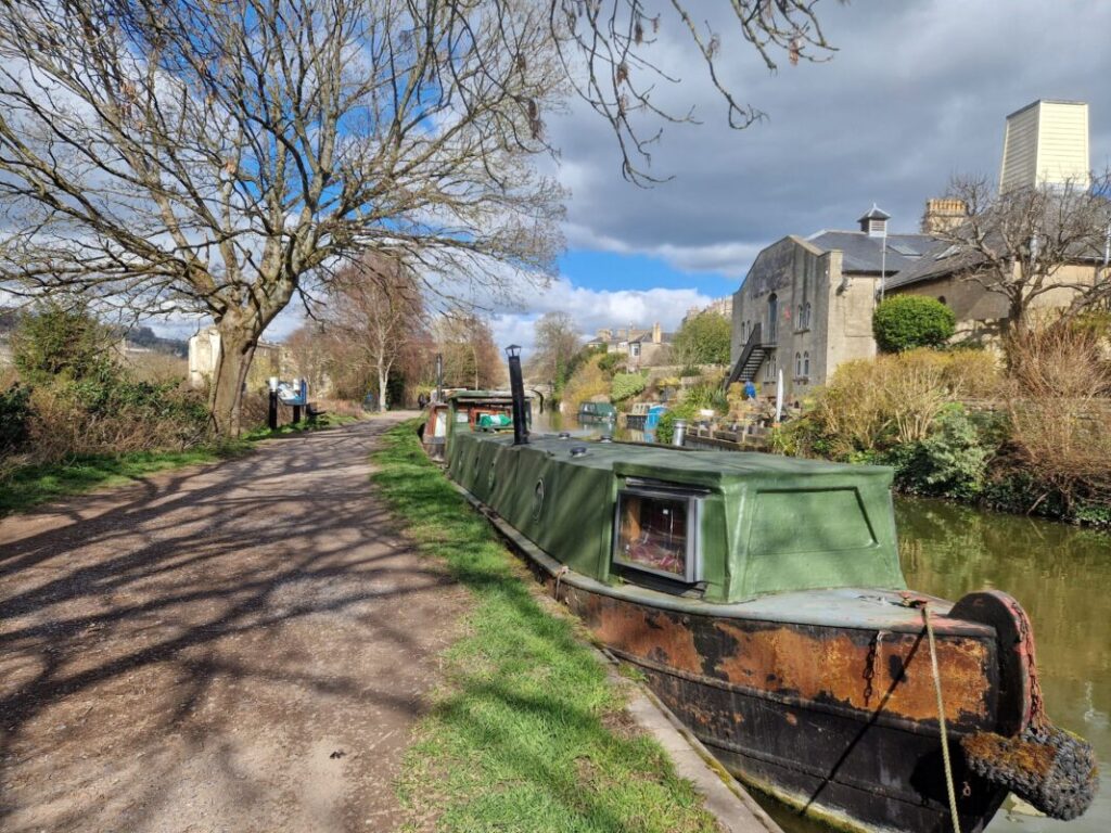 A canal boat moored under a tree next to a tow path in the city of Bath