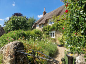 A traditional thatched cottage and cottage garden behind a gate leading to the garden.