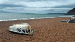 Photo of a shingle beach with an upturned boat on the shore and the sea stretching off into the distance.