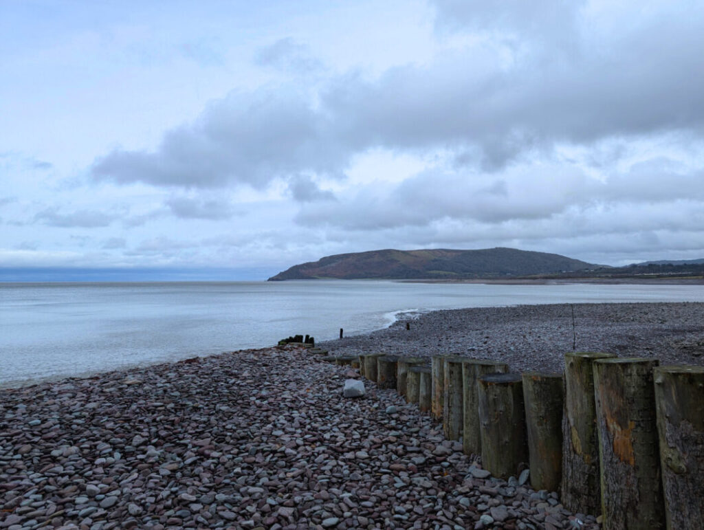 A grey shingle beach running down to the sea with a groyne to the right