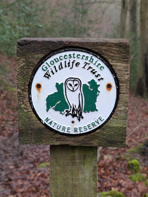 Signpost with a badge showing Gloucestershire Wildlife Trust Nature Reserve