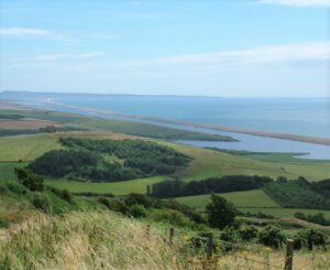 View of rolling green landscape with Chesil Beach in the distance.
