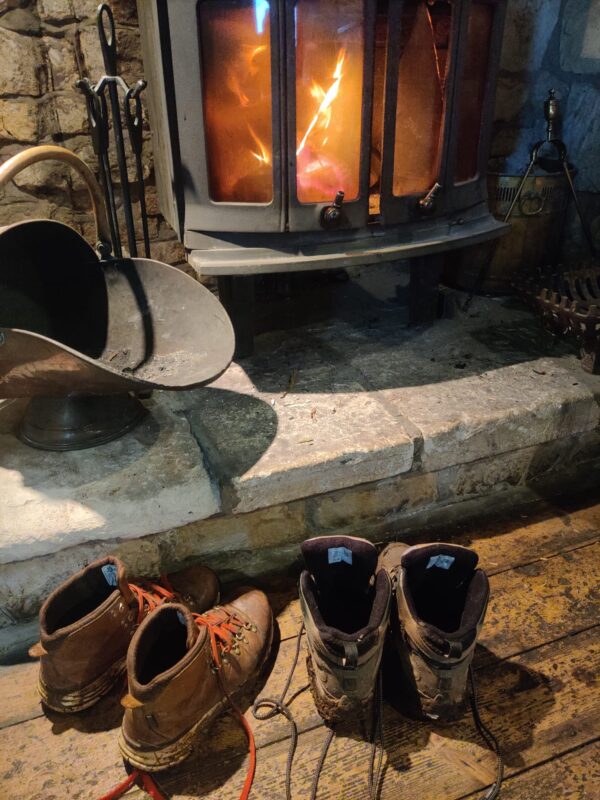 Two pairs of walking boots in front of a lit wood burning stove