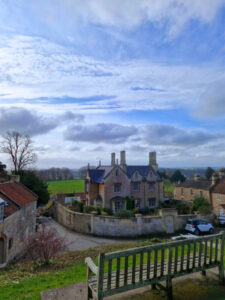 View over a grand house and the countryside beyond, with a bench in the foreground