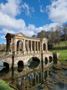 Ornate Palladian bridge with stone columns reflected in the still waters of a lake