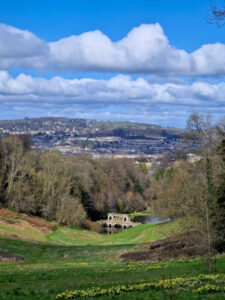 View of an ornate Palladian bridge set in parkland with the city of Bath in the background