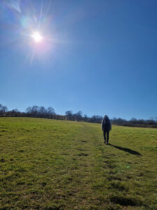 Person walking up a field. There are trees on the horizon and the sun is shining in a cloudless sky.