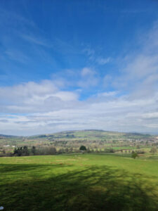 View of the hills from the top of a field; the green field stretching out below and hills in the distance.