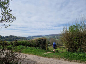 A person leaning on a wooden gate next to a dirt track. They are looking out over the countryside.