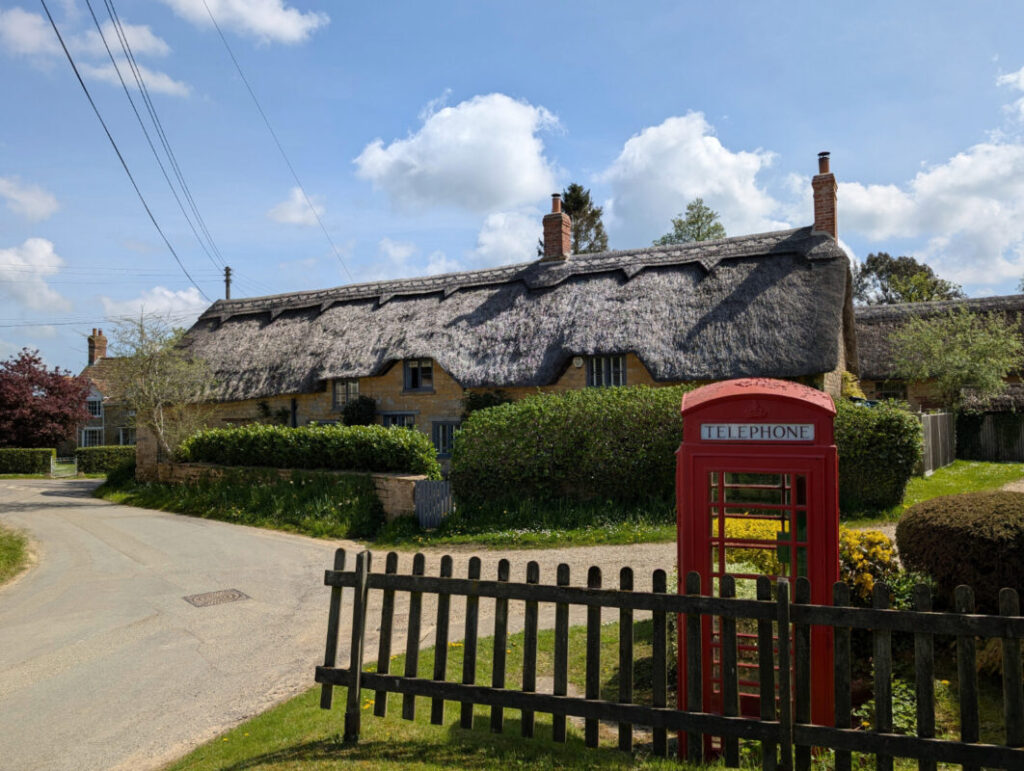 Photo of an old thatched cottage, in front, a quiet country lane, red telephone box and picket fence