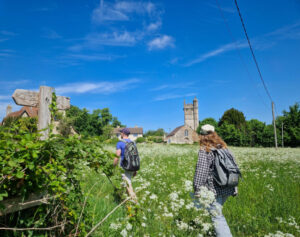 A man and a woman walking through a field past a finger post, with church in the background