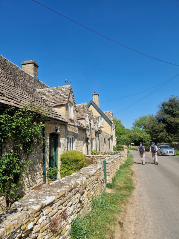 Two people walking along a lane next to a row of Cotswolds cottages
