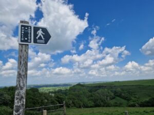 Footpath sign against a blue sky and countryside stretching off into the distance