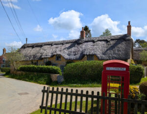 Photo of an old thatched cottage, in front, a quiet country lane, red telephone box and picket fence