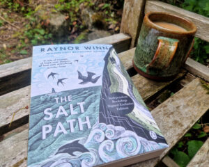 Photo of the book The Salt Path on a garden bench next to a mug of tea.