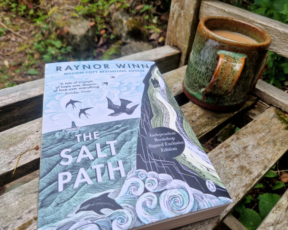 Photo of the book The Salt Path on a garden bench next to a mug of tea.