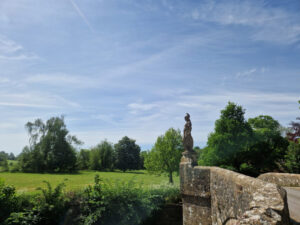 Photo of an old stone bridge with the figure of Brittania stood over one of the arches with fields in the background