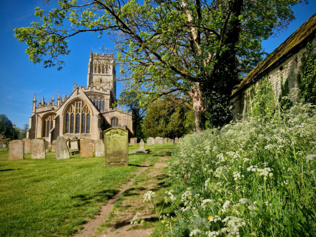 Photo of a grand Cotswolds church with cow parsley and a footpath in the foreground