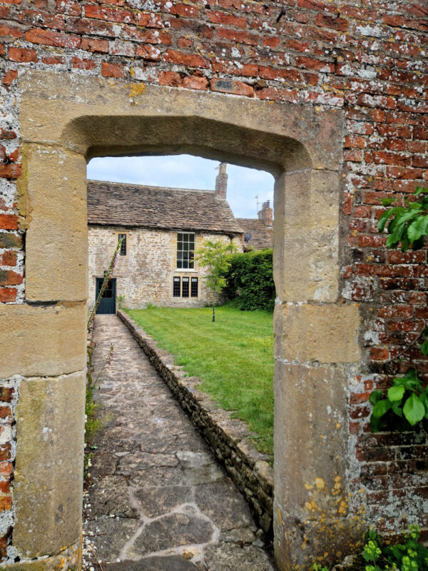 An old stone archway with a stone path leading to an old cottage.