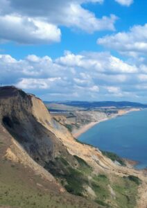 View of the Dorset coast from the top of a sea cliff. Blue sea to the right and the coast stretching off into the distance.