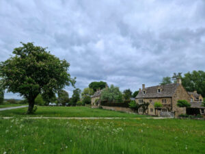 Scene from a Cotswolds village with a cottage on the right and horse chestnut tree on the left
