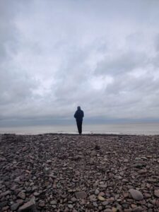 Silhouette of a person standing on a pebble beach with the sea stretching out into the horizon