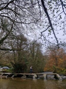 A hiker walking over an ancient stone bridge over a river in a wooded valley