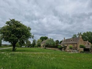 A classic Cotswolds stone cottage with a green and a horse chestnut tree in front.