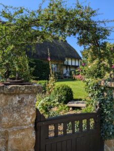 Traditional thatched cottage with a floral arch and gate in the foreground