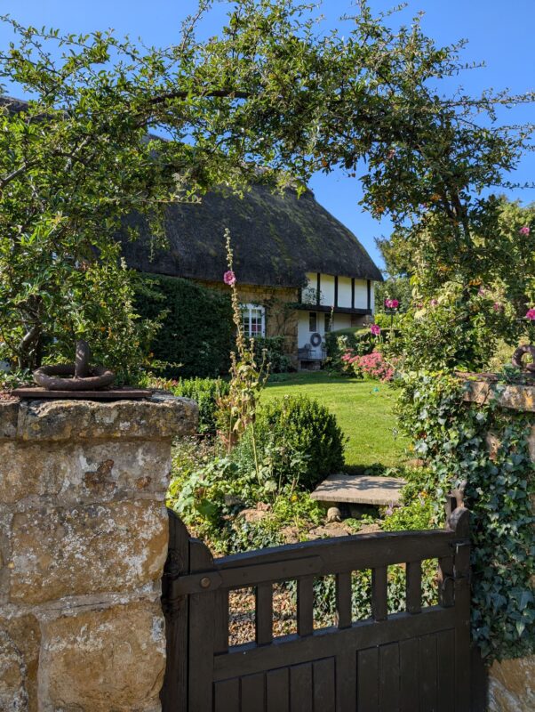 Traditional thatched cottage with a floral arch and gate in the foreground
