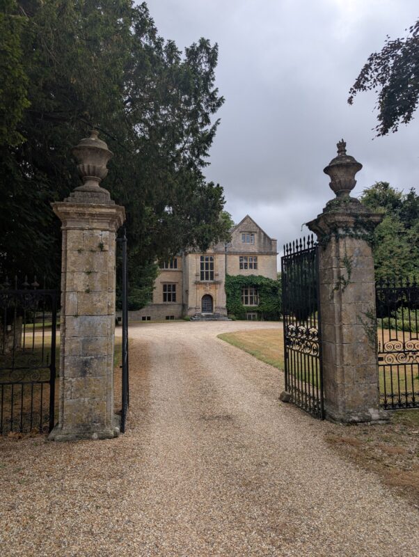 Stone and iron gates leading to a manor house, which can be seen in the background