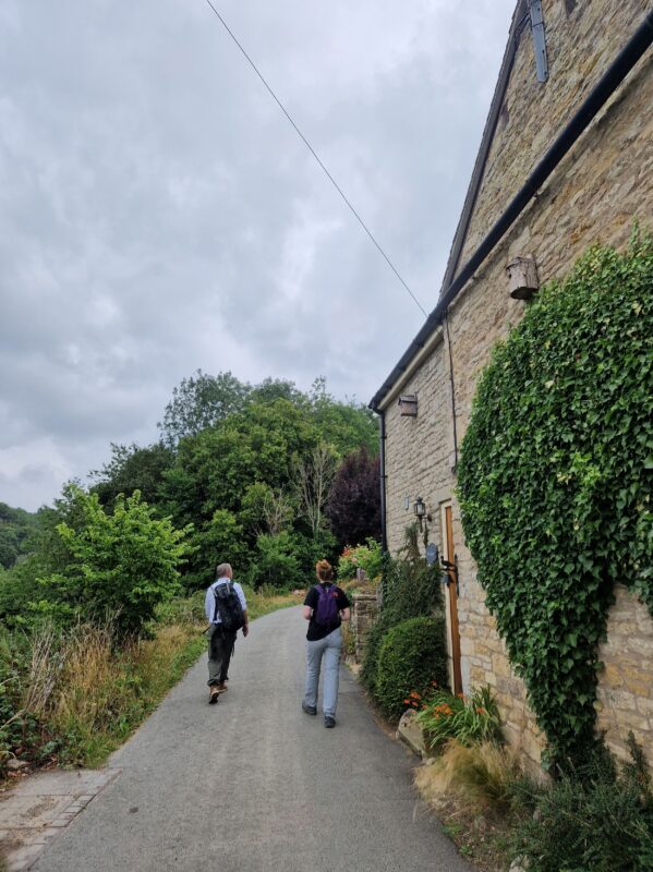 Two people walking along a quiet country lane next to an old cottage