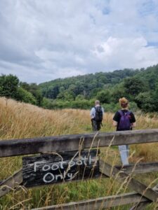 Two people walking in a field behind a fence with a hand-painted sign reading 'Footpath only'