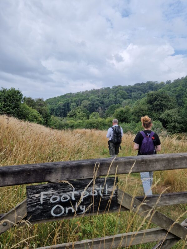 Two people walking in a field behind a fence with a hand-painted sign reading 'Footpath only'