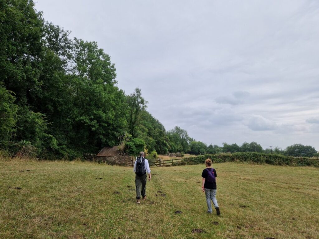 Two people walking across a field towards a gate next to a ramshackle old farm barn