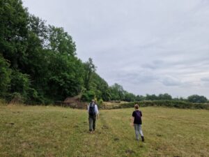 Two people walking across a field towards a gate next to a ramshackle old farm barn