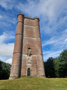 An imposing red brick tower with turrets shown against a bright blue sky