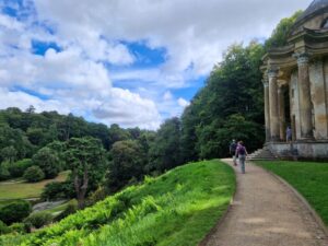Two walkers walking on a gravel path in a landscaped garden past a temple