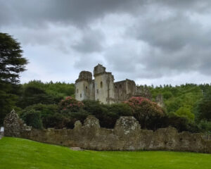 An ancient ruined castle against a moody sky with an old stone wall and grass in the foreground