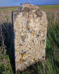 An ancient stone mile marker covered in lichen with barely legible script on it