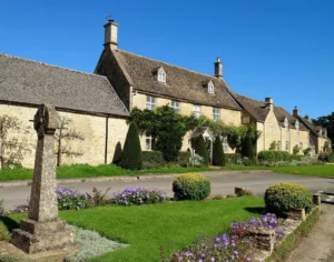 A quaint English village with a row of slate cottages and a commemorative cross on a small village green