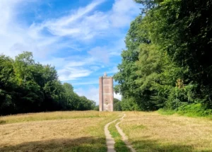 A Victorian folly in the English countryside with a footpath leading up to the building through a field with trees on each side.