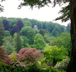 A beautifully landscaped garden full of trees and shrubs with a Greek-inspired temple on a hill in the background and a Palladian bridge over a lake in the centre