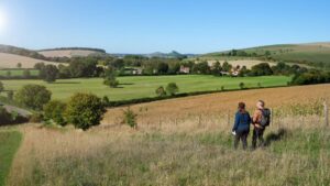 Photo of Alison & David Howell standing on a small hill, the countryside rolling away into the distance