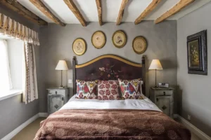Double room in a cosy country inn; there are oak beams on the ceiling and old paintings on the wall above an impressive double bed.