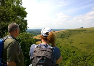 Two hikers pause on a ridge in South West England to look at rolling hills and fields stretching off into the distance.