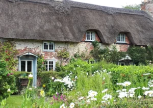 A traditional thatched cottage in South West England with a cottage garden full of flowers.