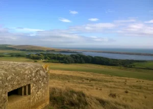 View of the South West Coast in England from a hill inland. There is a pillbox in the right corner, and fields stretching downhill to the sea.