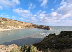 Image of Lulworth Cove on a sunny day: A large natural bay surrounded by cliffs where the South West Coast Path runs.