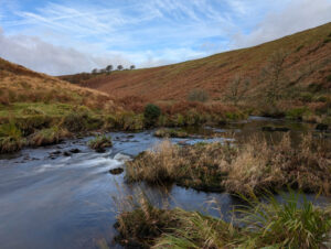 Exmoor in autumn with a river winding its way through the moor with hills banking off to the right and left.